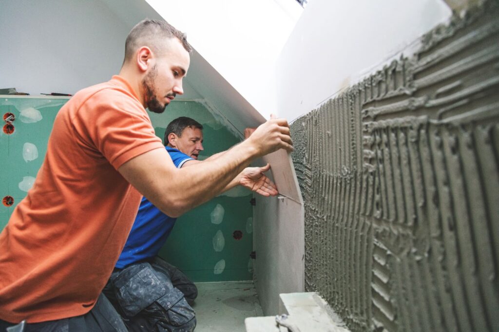 Two men working on a wall with cement during a bathroom remodel, focusing on countertops and overall remodel