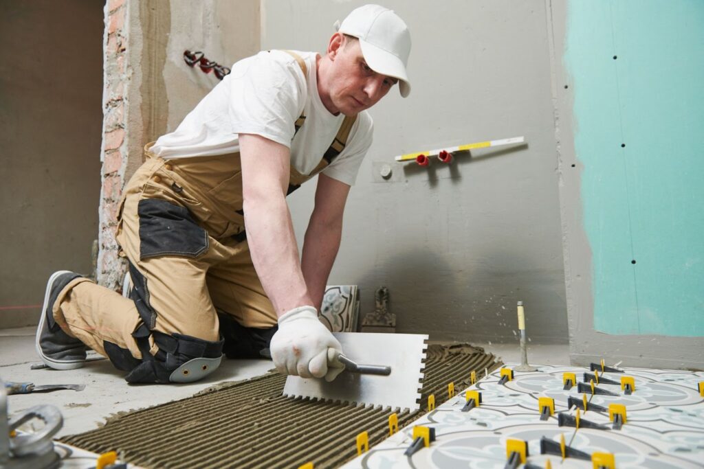 A man skillfully laying tiles on the floor during a bathroom renovation, transforming your bathroom.